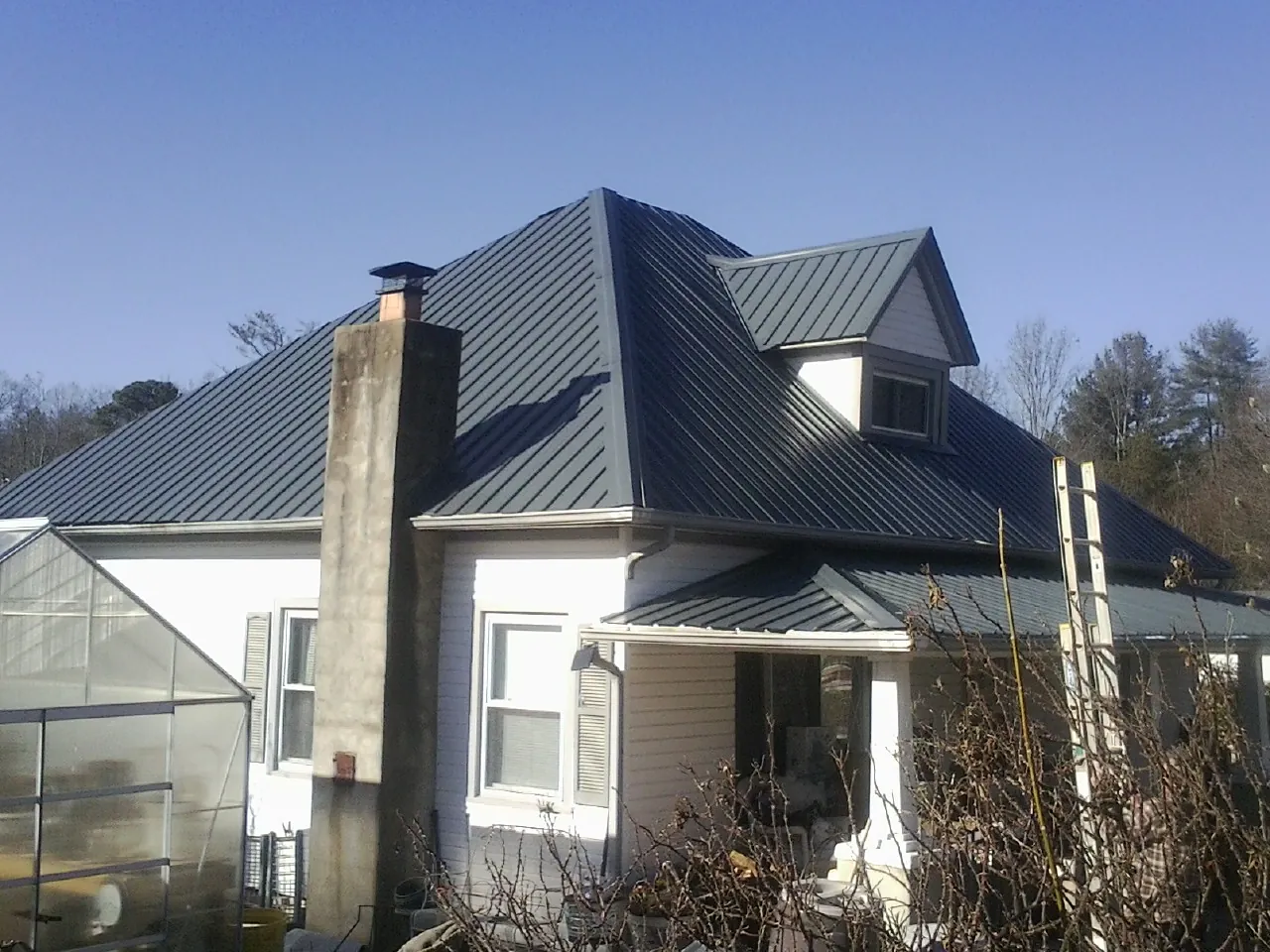 Dark blue standing seam metal roof on a white farmhouse with dormer — Slate & Tile Roof Repair by Roofing Brothers in Casa Blanca