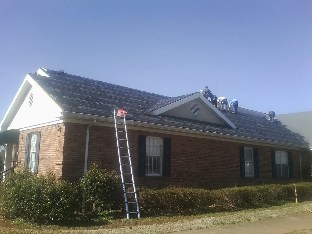 Crew tearing shingles off a brick ranch roof with a ladder set — Metal Roof Repair work by our crew in Casa Blanca