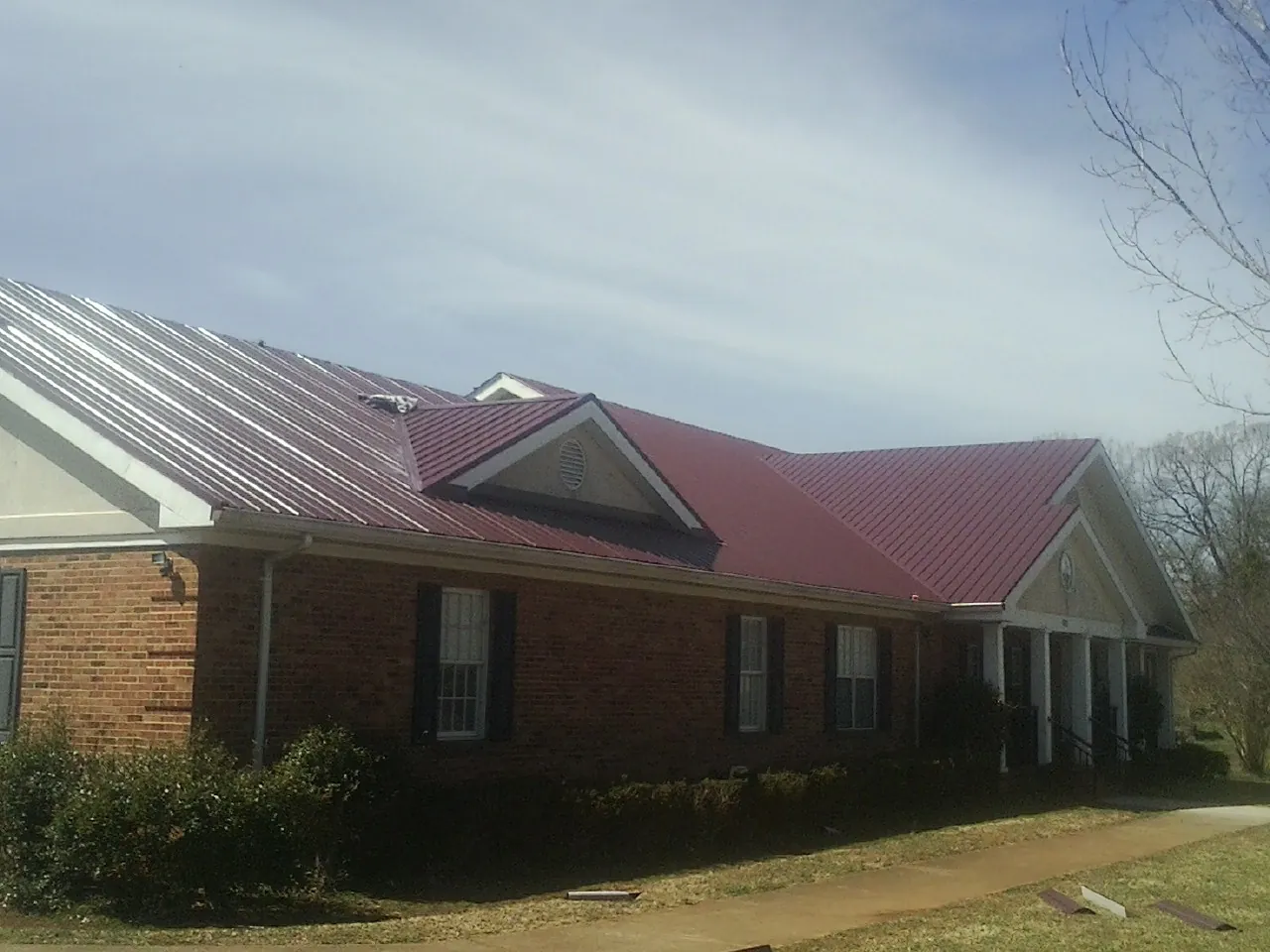 Red metal roof with gabled entries on a long brick building, from a Hail Damage Roof Repair job in Casa Blanca