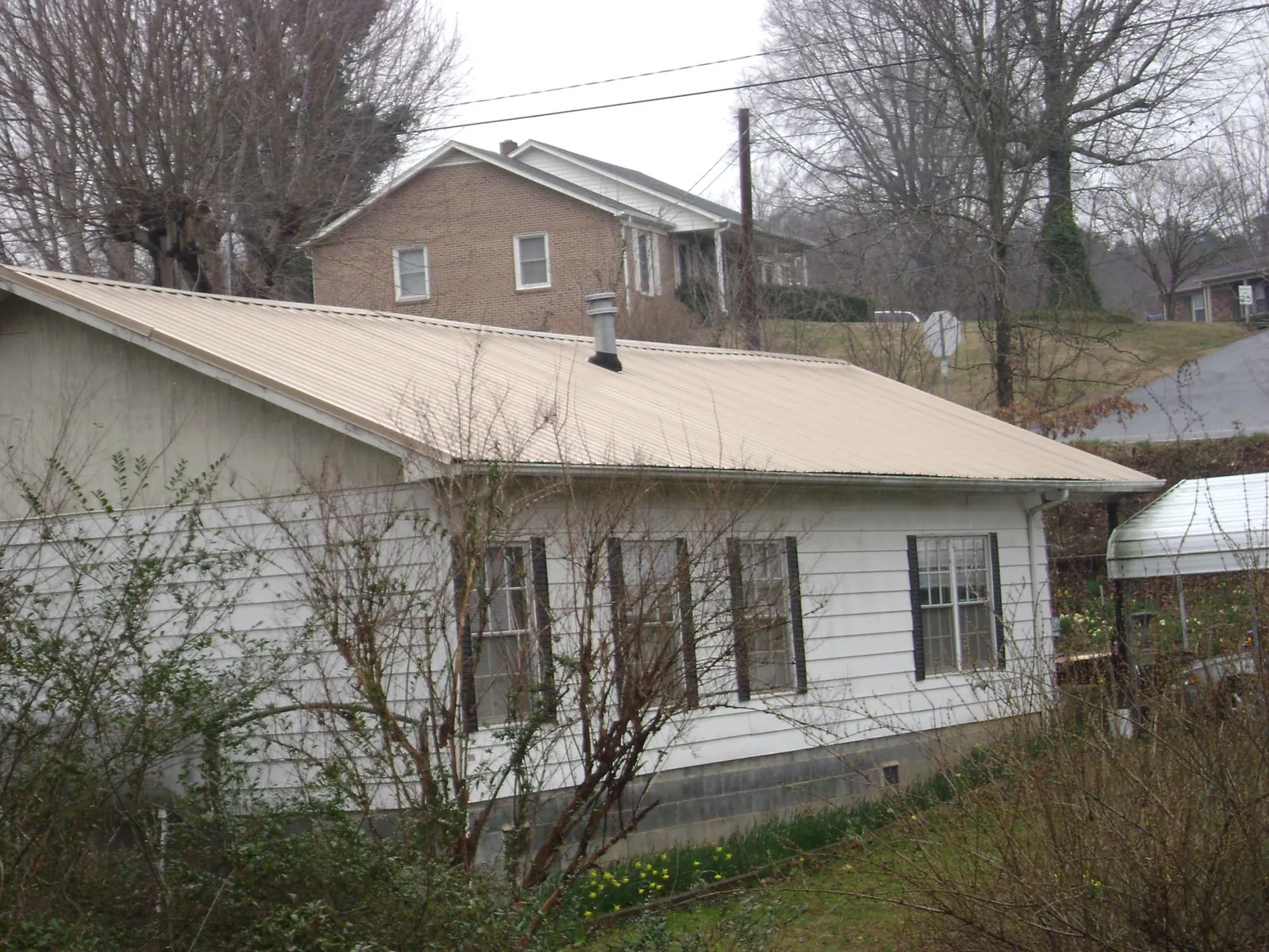 Tan metal roof on a white sided house set into a hillside — Commercial Roofing by Roofing Brothers in Casa Blanca